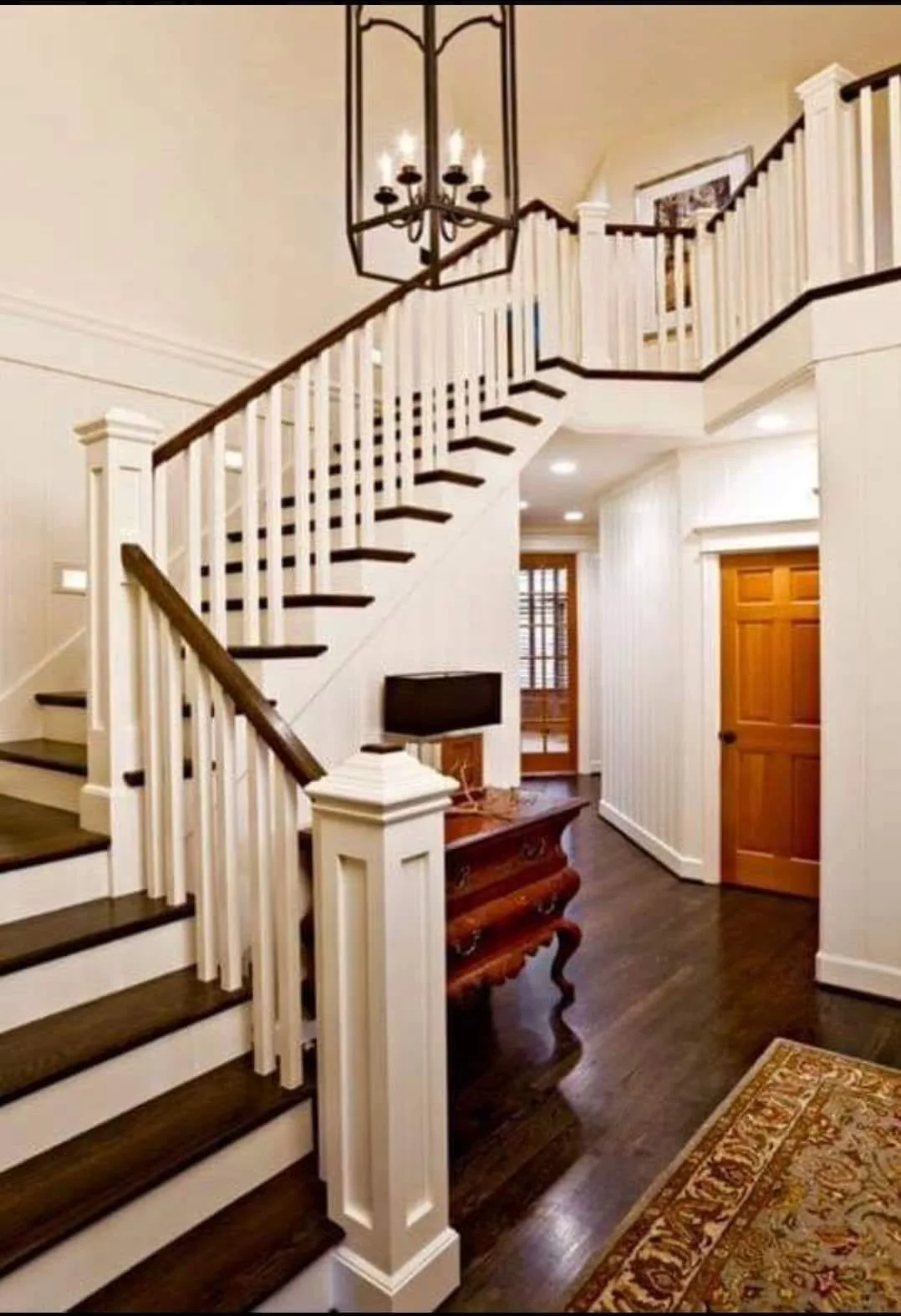 A wide view of a completed interior staircase and wood refinishing project featuring dark stained steps, white balusters, and varnished wooden doors.