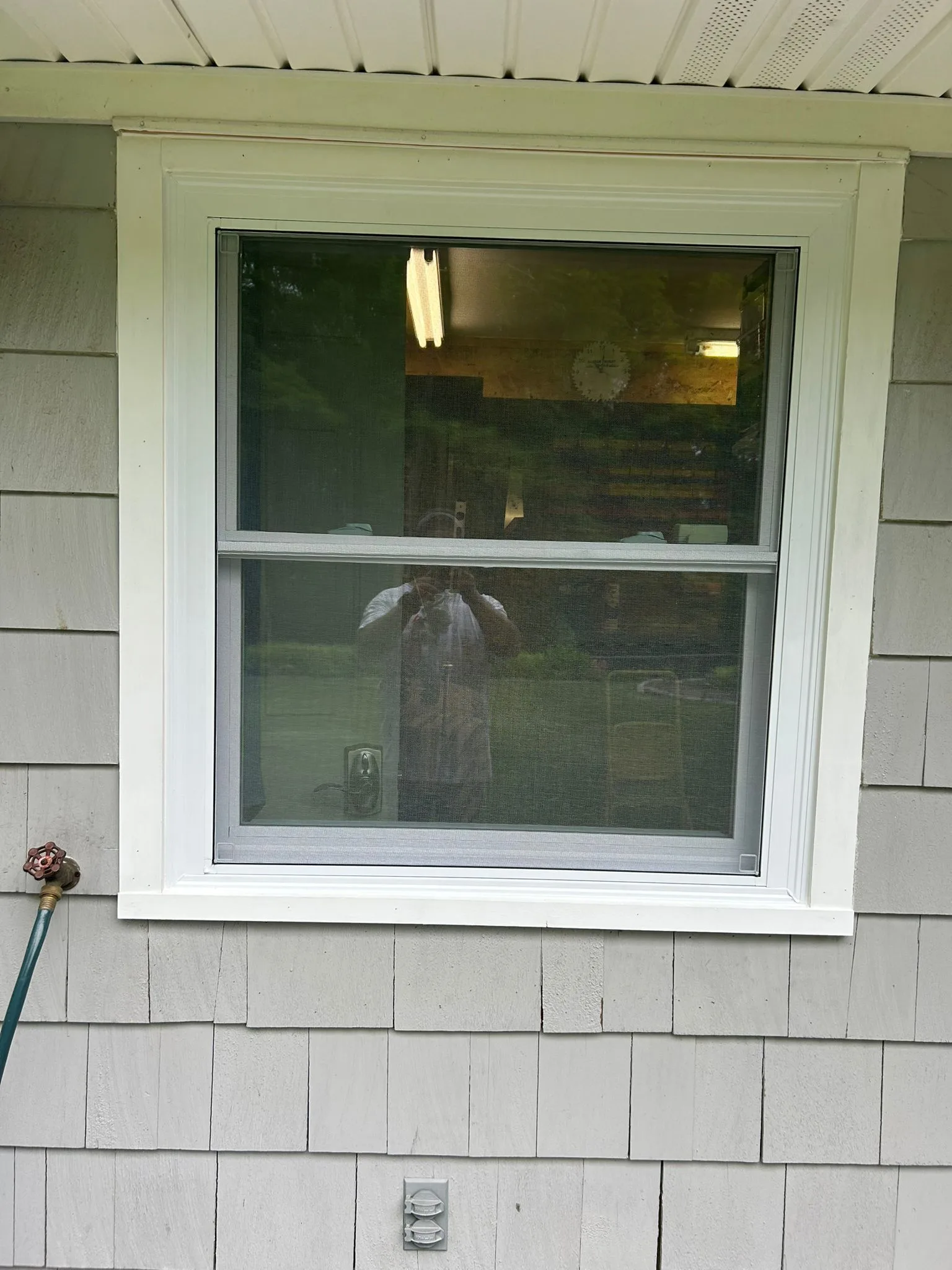 Exterior detail of a professional window installation showing the white casing and screen against gray cedar shingle siding.