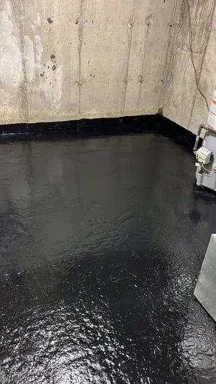 Close-up perspective of the finished, texturized black basement waterproofing coating along a foundation wall, detailing a pipe seal.