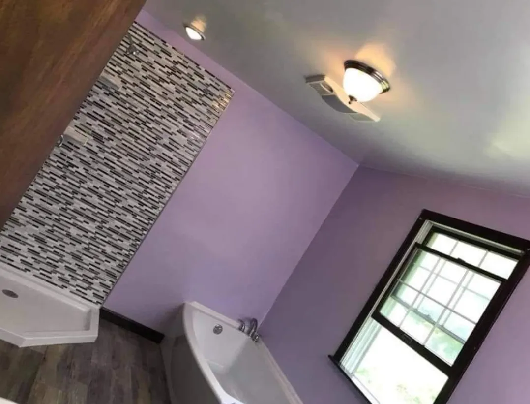 The completed full bathroom renovation, featuring new lavender walls, dark plank flooring, updated ceiling lights, and the modern mosaic shower tile.