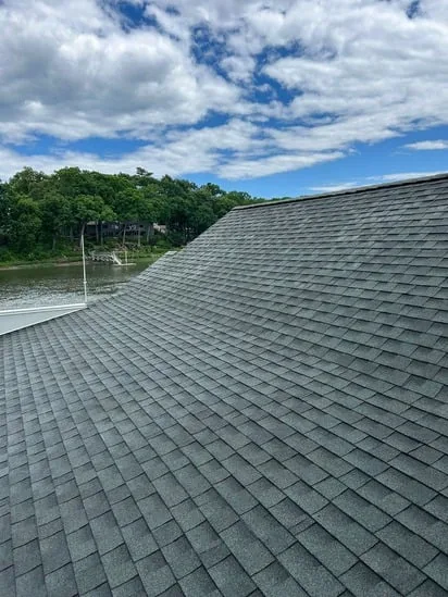 A comprehensive view of the entire gray shingle roofline and the cleaned gutter system, highlighting the proper drainage path established by the residential roof gutter service.